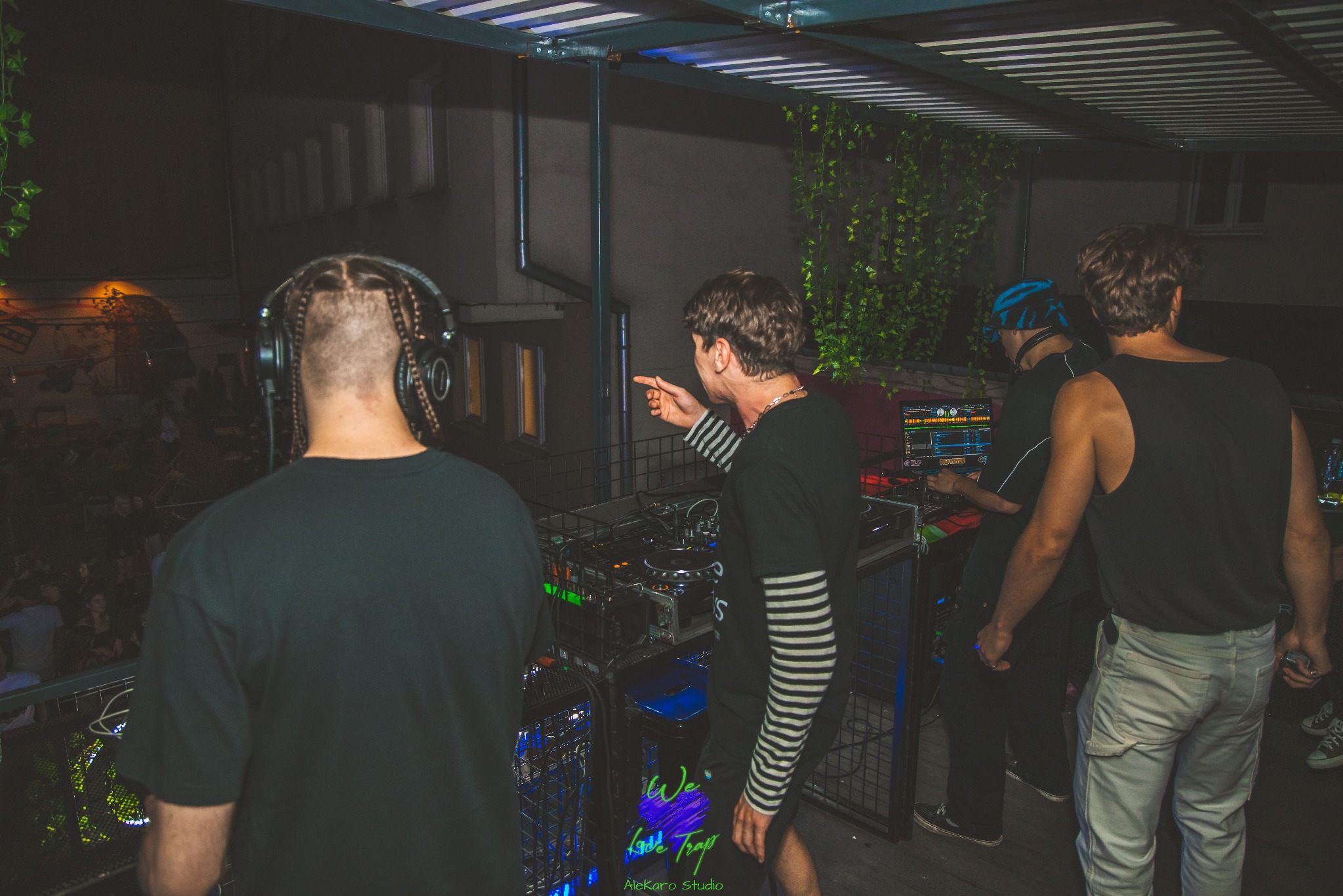 DJ-e grają muzykę na imprezie plenerowej, widoczny sprzęt DJ-ski, oświetlenie i publiczność w tle.