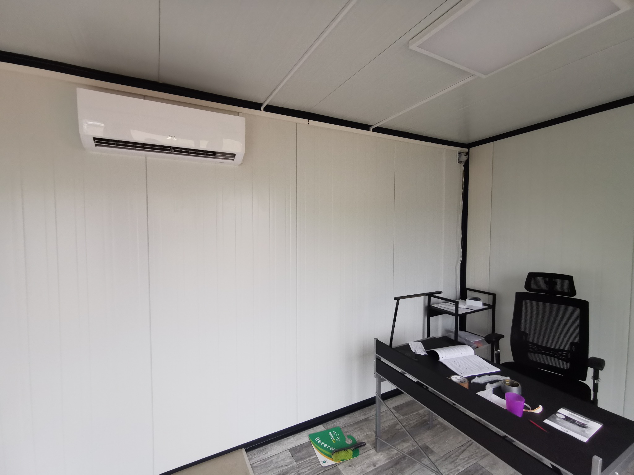 Biała jednostka klimatyzacyjna zamontowana na ścianie w minimalistycznym biurze w Warszawie, z widocznym biurkiem i krzesłem biurowym w tle.