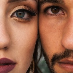 Maggieem studio - Zbliżenie na twarze pary: kobieta z niebieskim okiem, złotym makijażem i bordową szminką styka się nosem z mężczyzną o brązowym oku i brodzie.