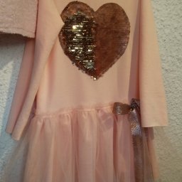 Zakład Krawiecki - Jasnoróżowa sukienka dziewczęca z cekinowym sercem i tiulowym dołem, zawieszona na wieszaku.