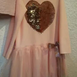 Jasnoróżowa sukienka dziewczęca z cekinowym sercem i tiulowym dołem, zawieszona na wieszaku.
