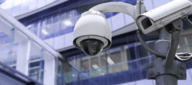 Dwie kamery przemysłowe na słupie, z nowoczesnym budynkiem biurowym w tle.