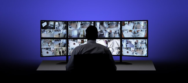 Operator monitoringu siedzi przed trzema monitorami pokazującymi obraz z kamer CCTV wewnątrz budynku.