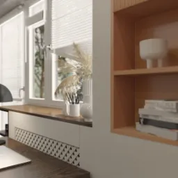 Jasne biuro domowe z drewnianym biurkiem, laptopem, lampą w stylu retro, półkami z książkami i dekoracjami, oraz oknem z widokiem na zieleń.