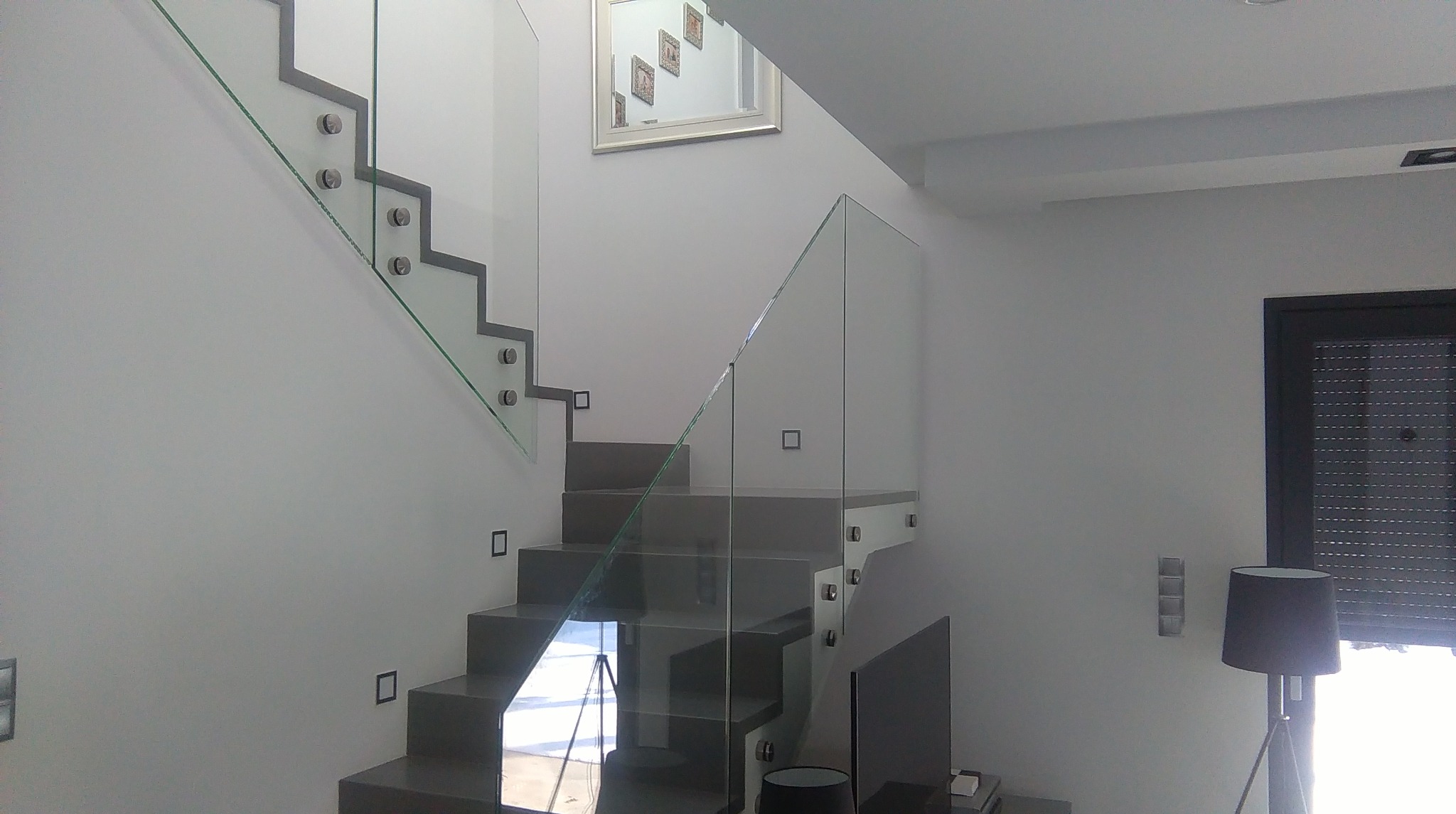 Nowoczesne schody z szarymi stopniami i szklaną balustradą mocowaną na metalowych uchwytach, oświetlenie schodowe, minimalistyczny design.