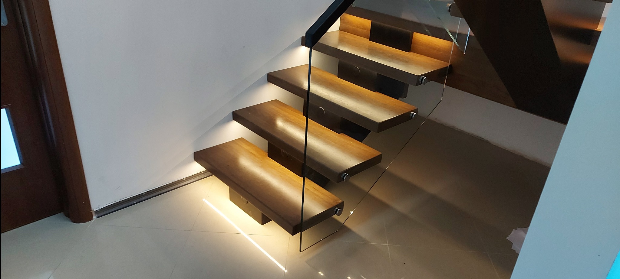 Nowoczesne schody wiszące z drewna z podświetleniem LED i szklaną balustradą, widok z góry. Minimalistyczny design i ciepłe światło podkreślają elegancję wnętrza.