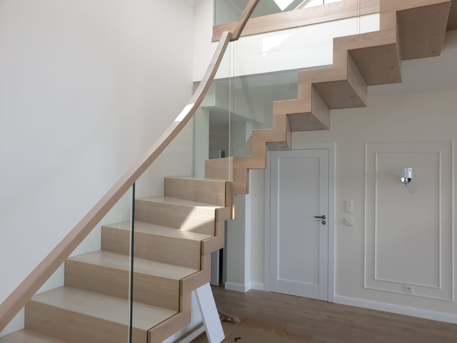 Nowoczesne schody drewniane z przeszkloną balustradą i jasnym drewnem, minimalistyczny design, widoczne detale wykończenia, eleganckie wnętrze.