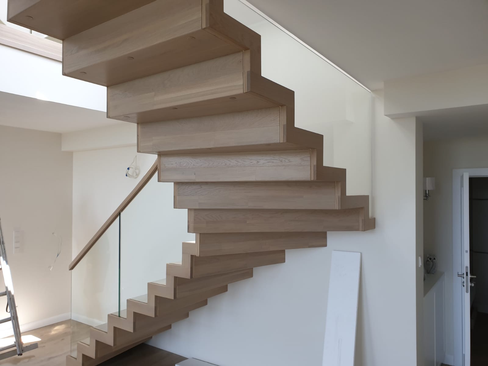 Nowoczesne schody z jasnego drewna, stopnie wspornikowe, szklana balustrada. Minimalistyczny design, białe ściany, naturalne światło.