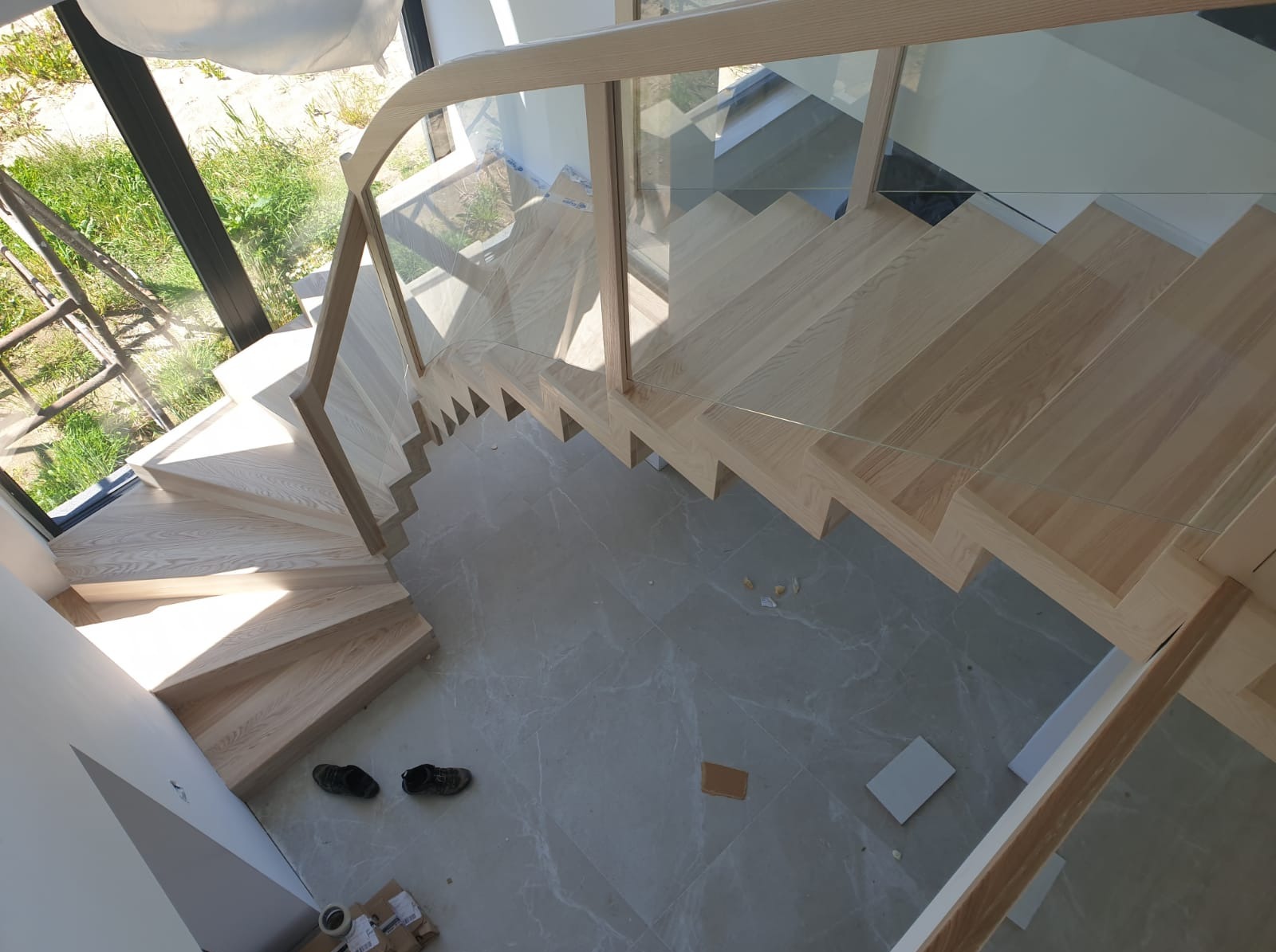 Koszalin: Spiralne schody z jasnego drewna, z nowoczesną szklaną balustradą, widziane z góry. Jasne wnętrze, marmurowe płytki podłogowe.