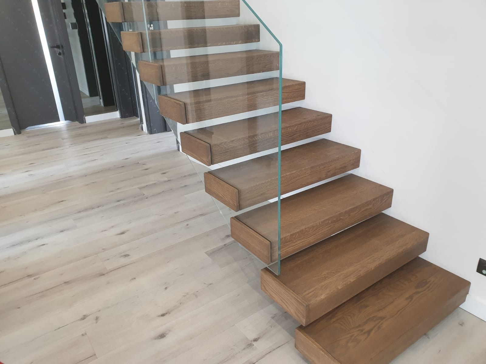 Nowoczesne schody z drewnianymi stopniami i szklaną barierką, widok z dołu, jasne wnętrze, minimalistyczny design, parkiet w tle.