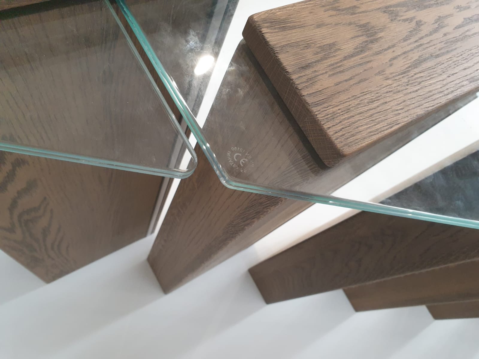 Szczegółowe ujęcie schodów drewnianych z balustradą szklaną, widok z dołu, podkreślający detale wykończenia i połączenie materiałów.