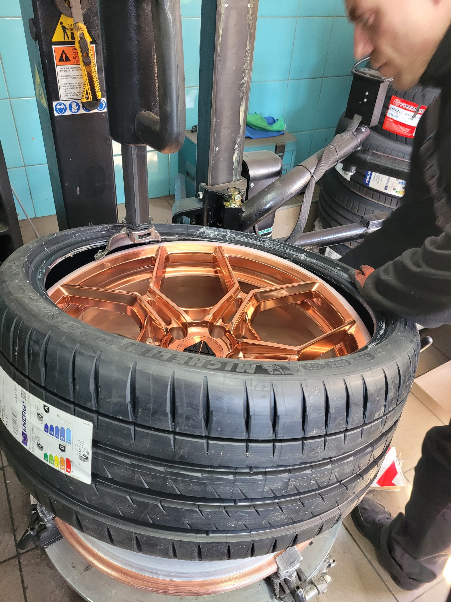 Montaż opony na felgę wulkanizacyjną o miedzianym kolorze, widoczna maszyna wulkanizacyjna i pracownik warsztatu.