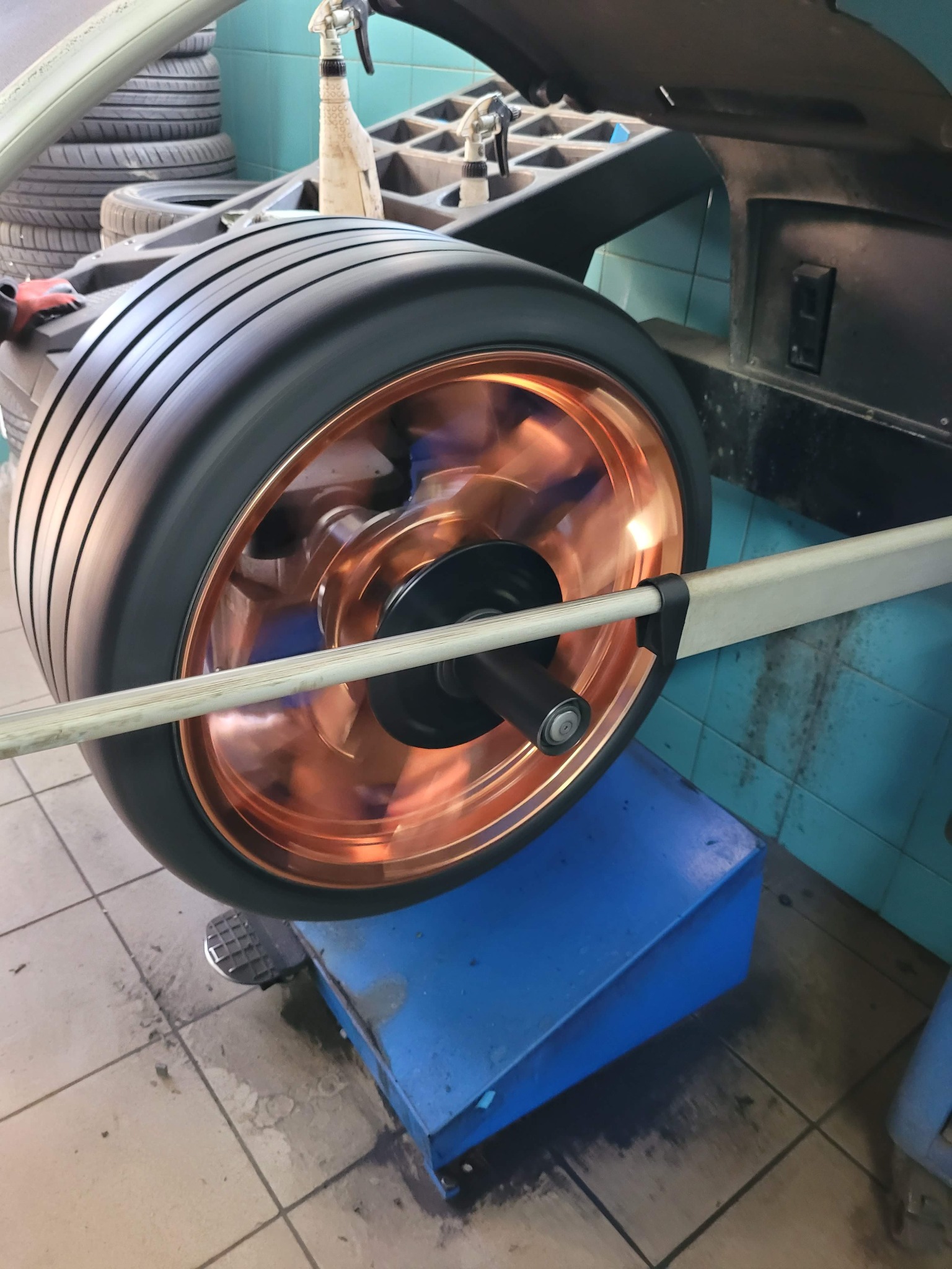 Wyważanie koła z miedzianą felgą na profesjonalnej wyważarce w warsztacie samochodowym, widoczne opony w tle.