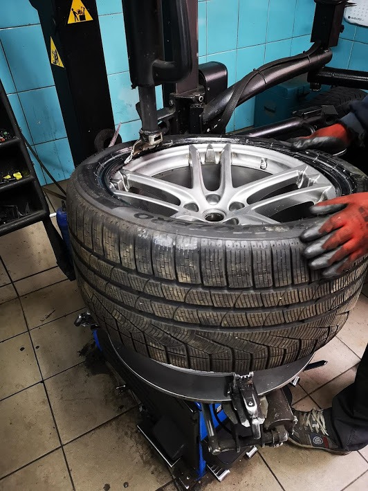 Wulkanizacja: Opona zimowa na feldze podczas montażu na maszynie w warsztacie, widoczne rękawice ochronne.