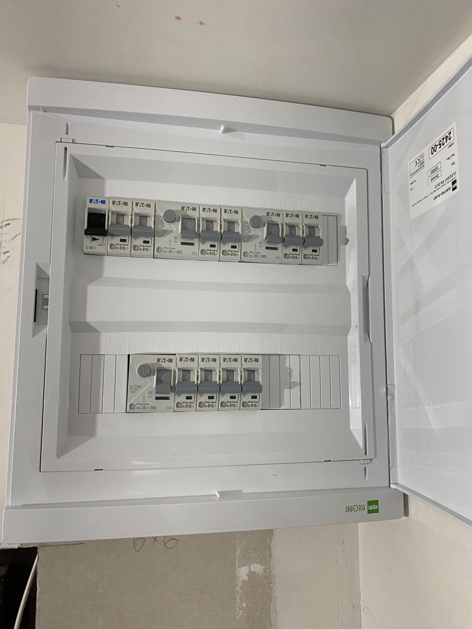 Otwarta skrzynka rozdzielcza z bezpiecznikami EATON, widoczne numery obwodów, zamontowana na ścianie w trakcie wykończenia.
