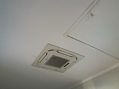 Kasetonowa jednostka klimatyzacji zamontowana w suficie podwieszanym z widocznym panelem dostępowym do instalacji.