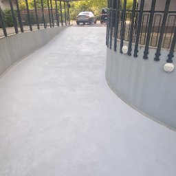 Epoxy3D - Biała, gładka posadzka wjazdowa do garażu podziemnego, z widocznymi lampami na ścianach i metalową barierką.