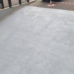 Epoxy3D - Świeżo wylana, jasnoszara powierzchnia z żywicy epoksydowej, zabezpieczona stożkami ostrzegawczymi i taśmą, widok z góry, z elementami metalowej balustrady.