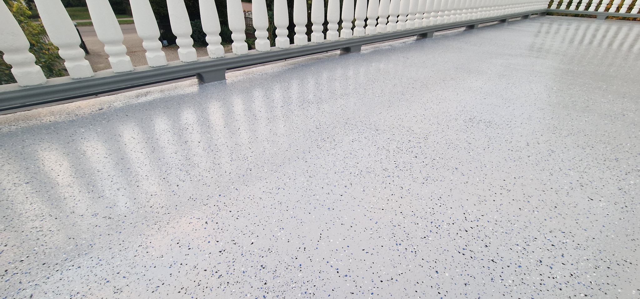 Jasnoszara posadzka z drobnymi, kolorowymi wtrąceniami na balkonie z białą balustradą, widok z góry.