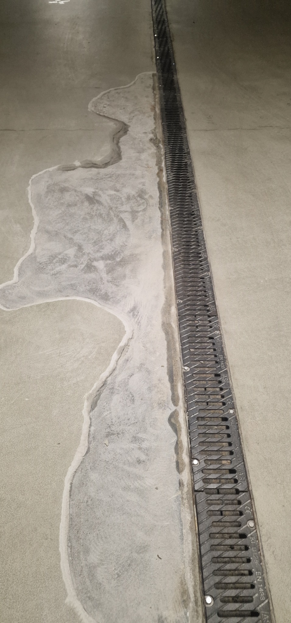 Szara posadzka przemysłowa z odpływem liniowym, widoczne ślady po wylewce samopoziomującej.