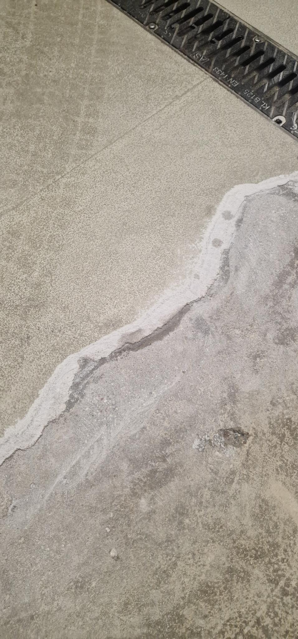 Szara, betonowa posadzka przemysłowa z widocznym odpływem liniowym i śladami po usunięciu plamy lub naprawie powierzchni