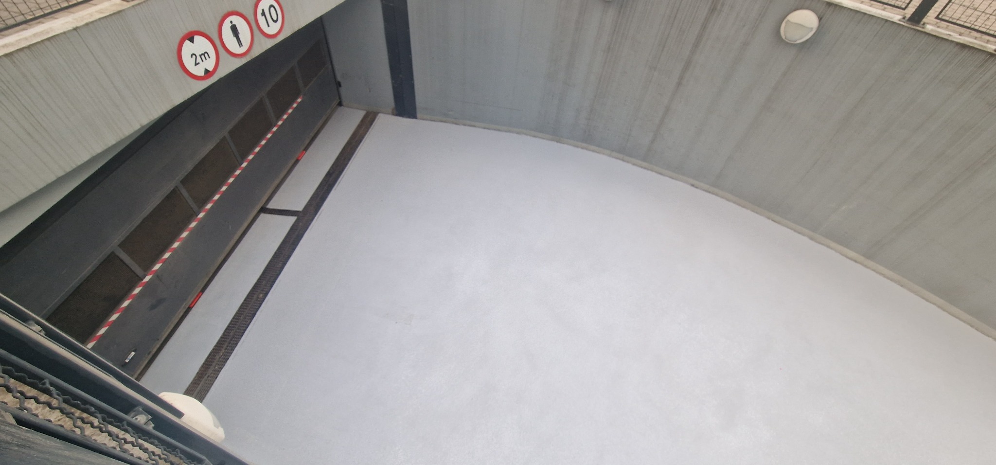 Jasnoszara, gładka posadzka w hali przemysłowej, widoczne znaki informacyjne na ścianie, perspektywa z dołu.