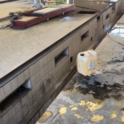 Clean Paradise - Wnętrze hali po umyciu, widoczne mokre plamy na posadzce, biało-żółty kanister z płynem czyszczącym oraz złożone metalowe elementy konstrukcyjne.