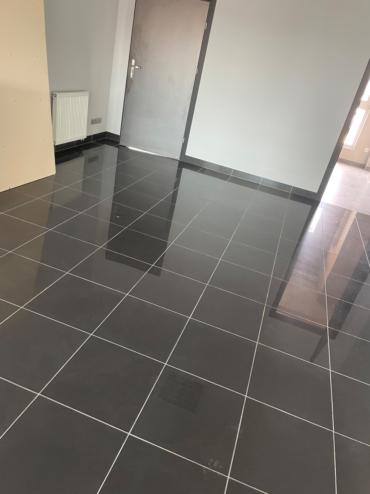 Błyszcząca czarna podłoga z płytek w nowym, pustym pomieszczeniu z grzejnikiem i drzwiami.