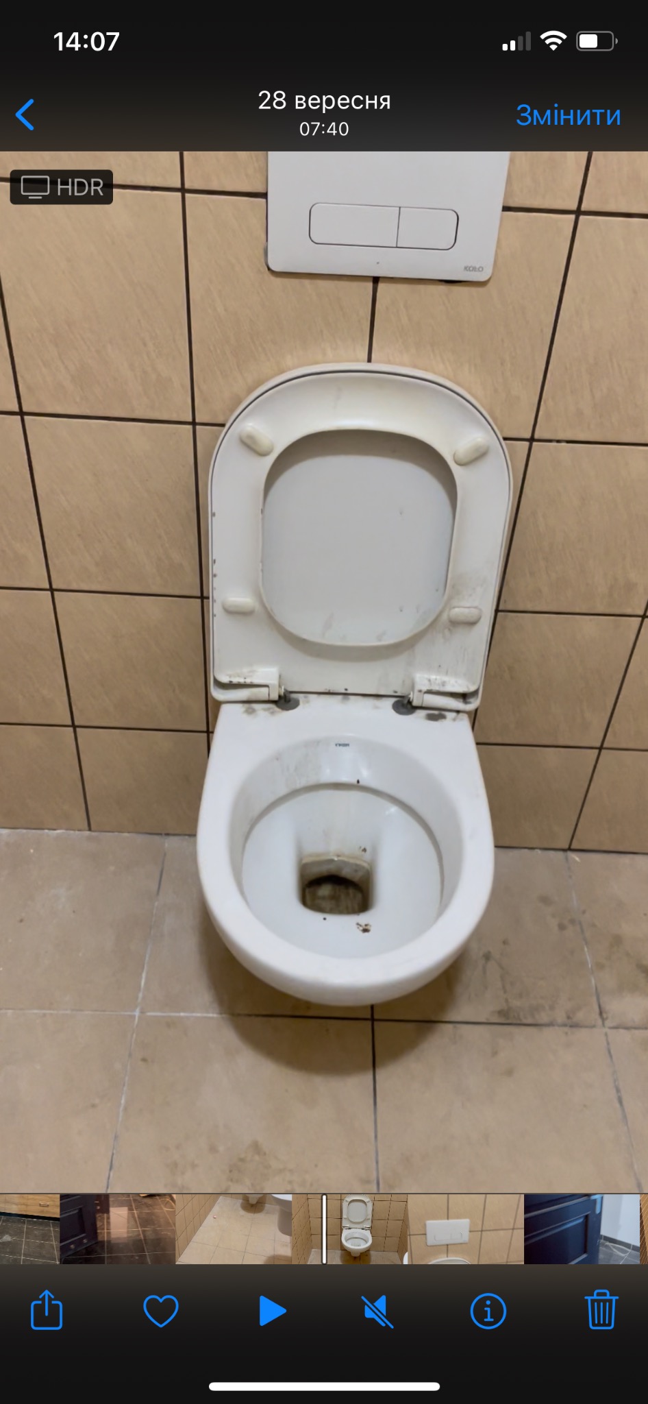 Widok z góry na brudną, otwartą muszlę klozetową w toalecie z beżowymi kafelkami.