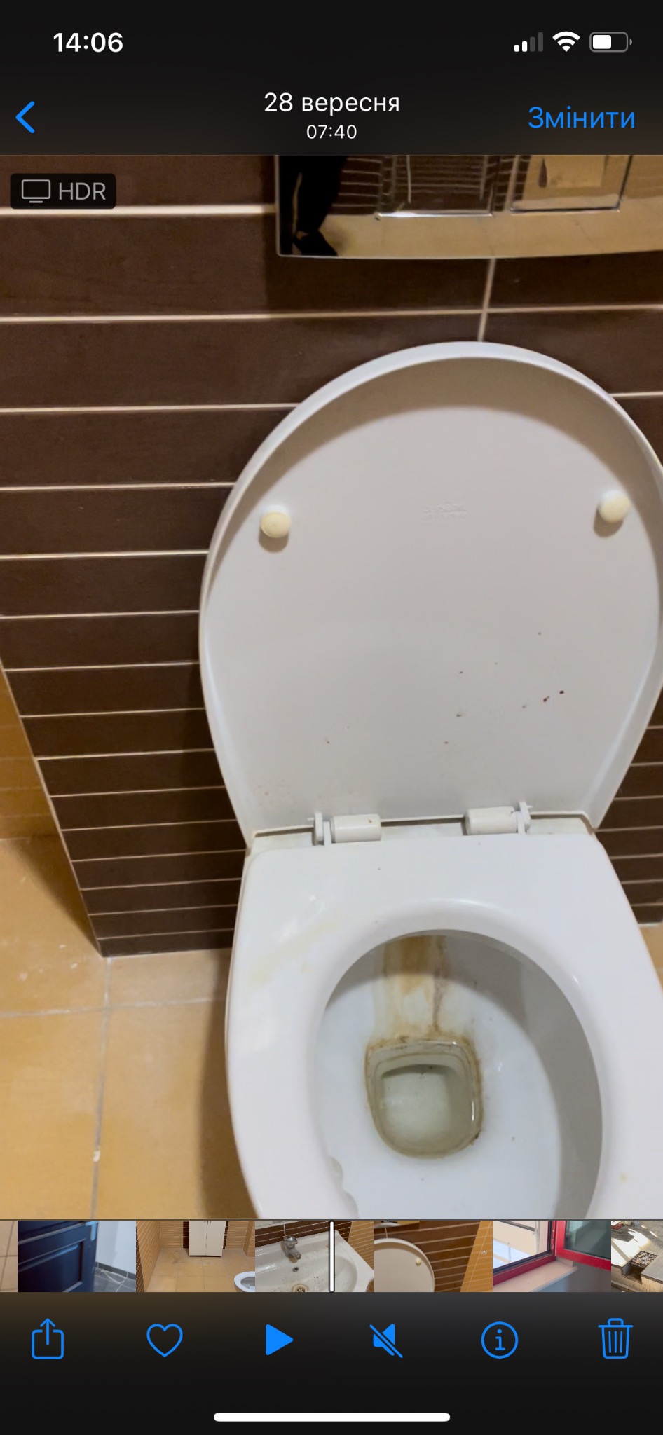 Zanieczyszczona muszla klozetowa z otwartą klapą, widoczne brązowe zacieki i osad, brązowe płytki na ścianie w tle.