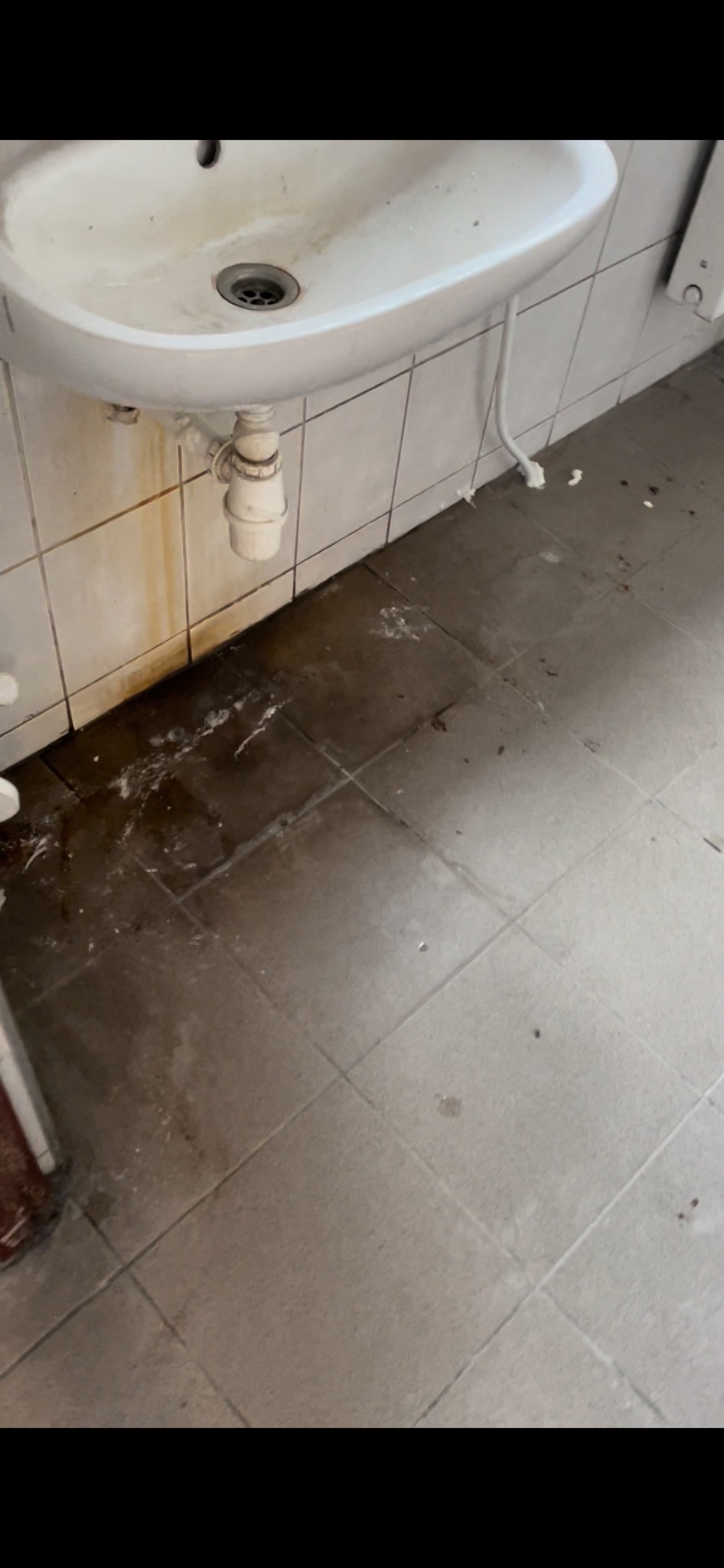 Zanieczyszczona umywalka i podłoga w łazience w Wielogórze, widoczne ślady rdzy i zabrudzenia na płytkach.