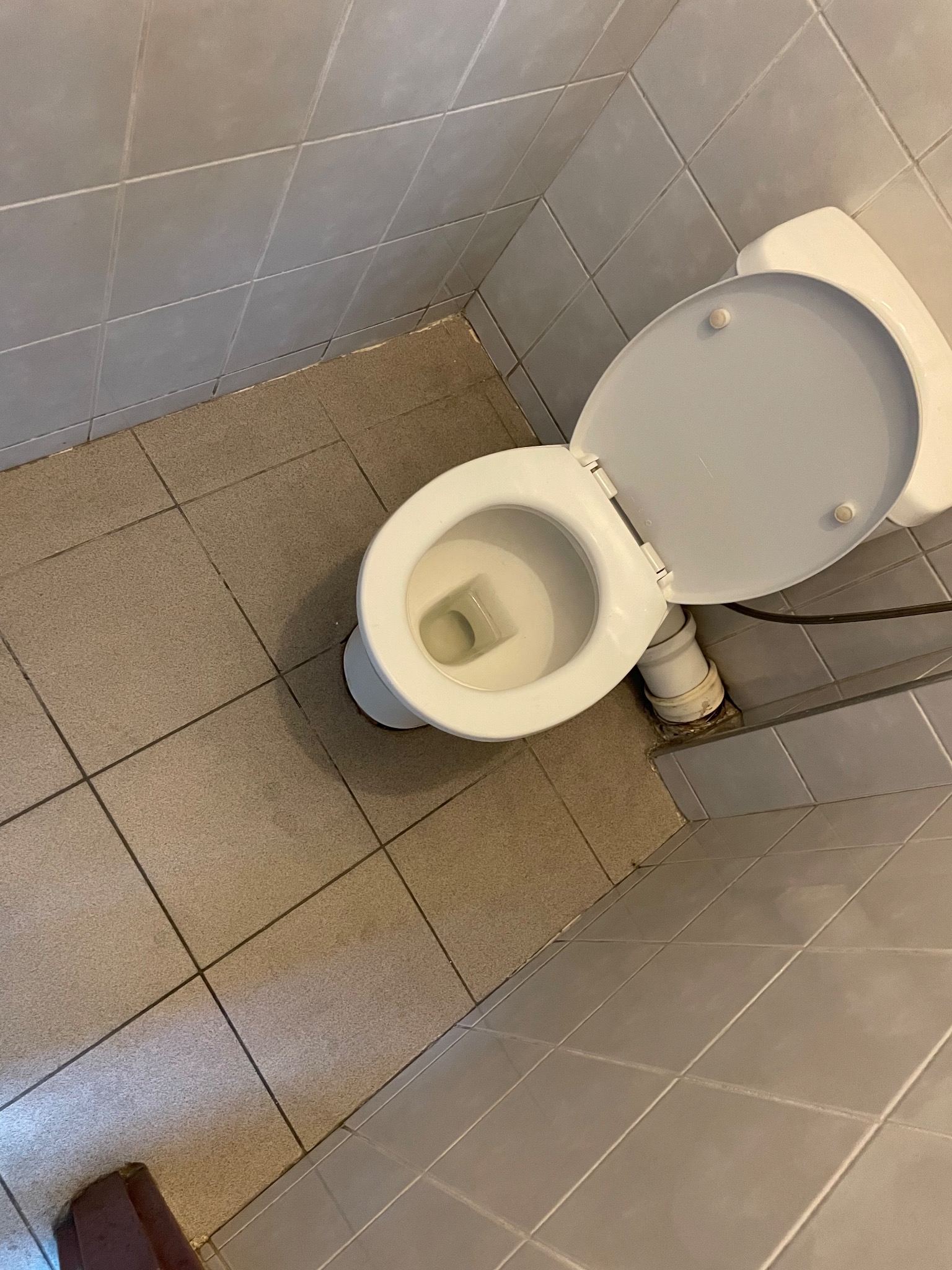 Toaleta z otwartą klapą w łazience wyłożonej szarą glazurą i brązowymi płytkami podłogowymi, widok z góry.