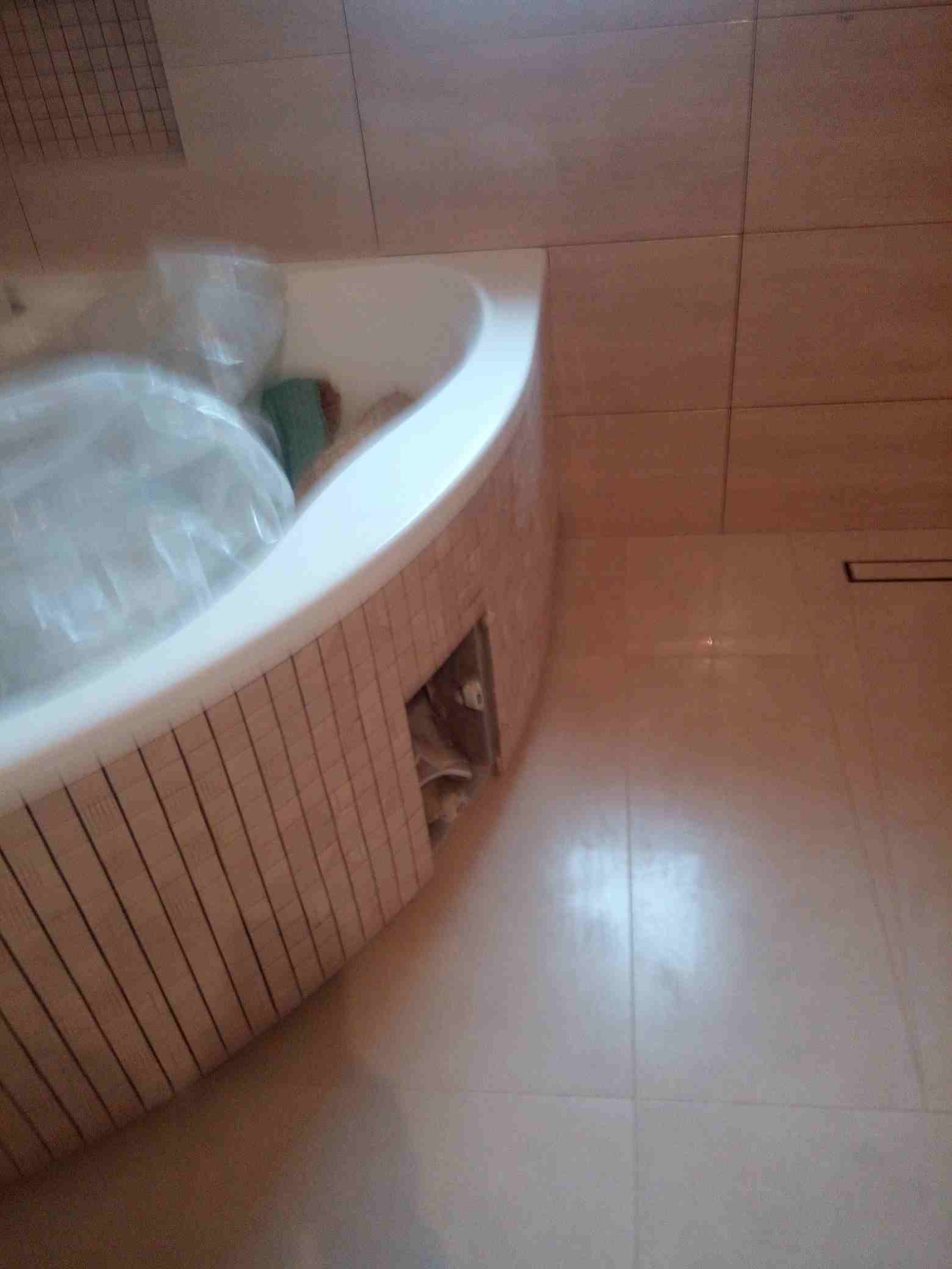 Obudowana płytkami wanna w trakcie remontu łazienki, widoczne zabezpieczenia folią, jasne płytki na podłodze i obudowie wanny.