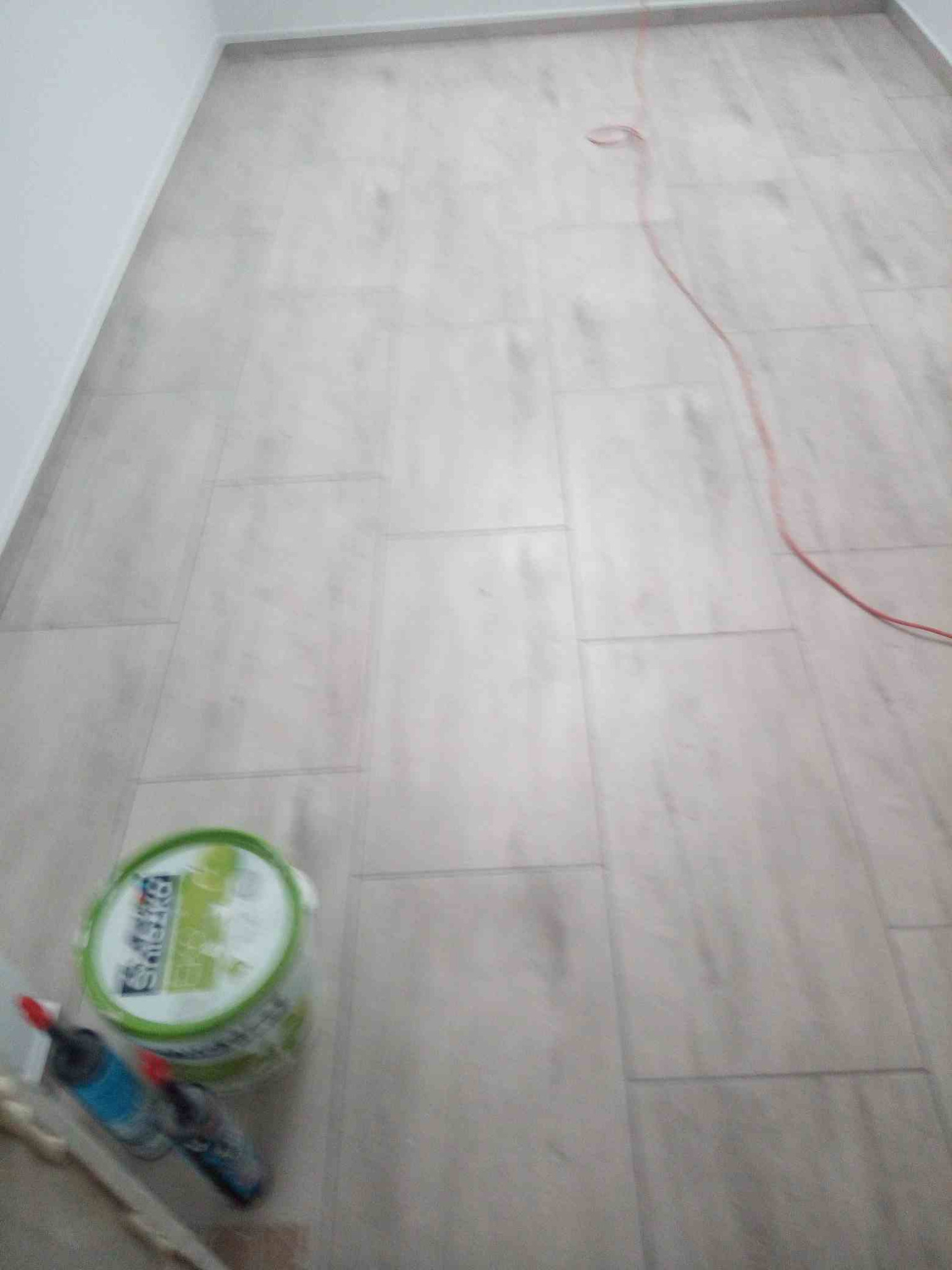 Świeżo położona podłoga z paneli imitujących drewno, widoczny pojemnik z farbą i narzędzia malarskie, czerwony kabel leżący na podłodze.