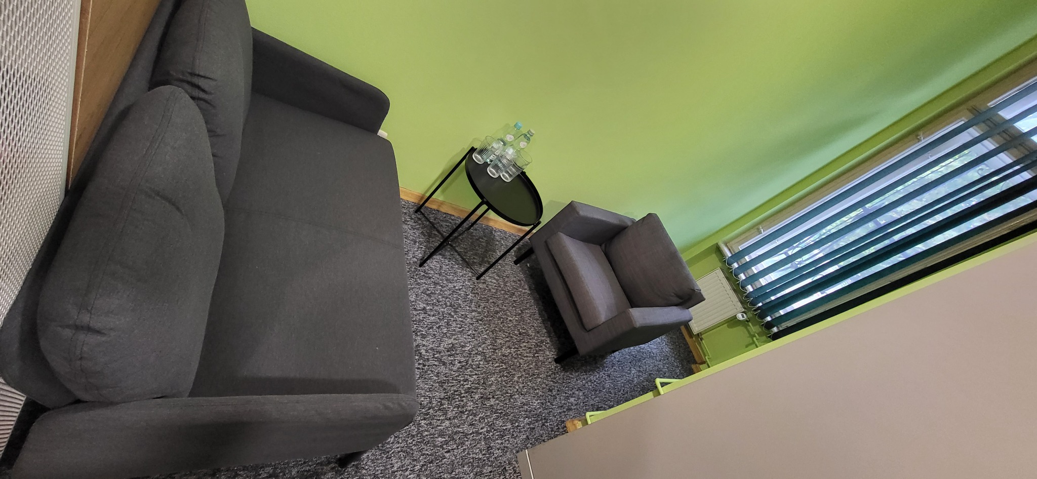 Wnętrze pokoju z szarą sofą, fotelem i stolikiem z wodą mineralną oraz szklankami, widok z góry.