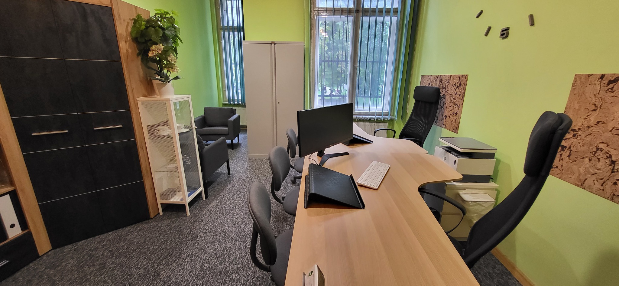 Nowoczesne biuro z zielonymi ścianami, biurkiem z komputerem, krzesłami biurowymi, szafą i elementami dekoracyjnymi.