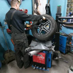 Mechanik w kombinezonie roboczym wymienia oponę Continental na feldze Mercedes-Benz na montażownicy VORTEC PRO MO-420 w warsztacie samochodowym. W tle widoczny kalendarz i spawarka.