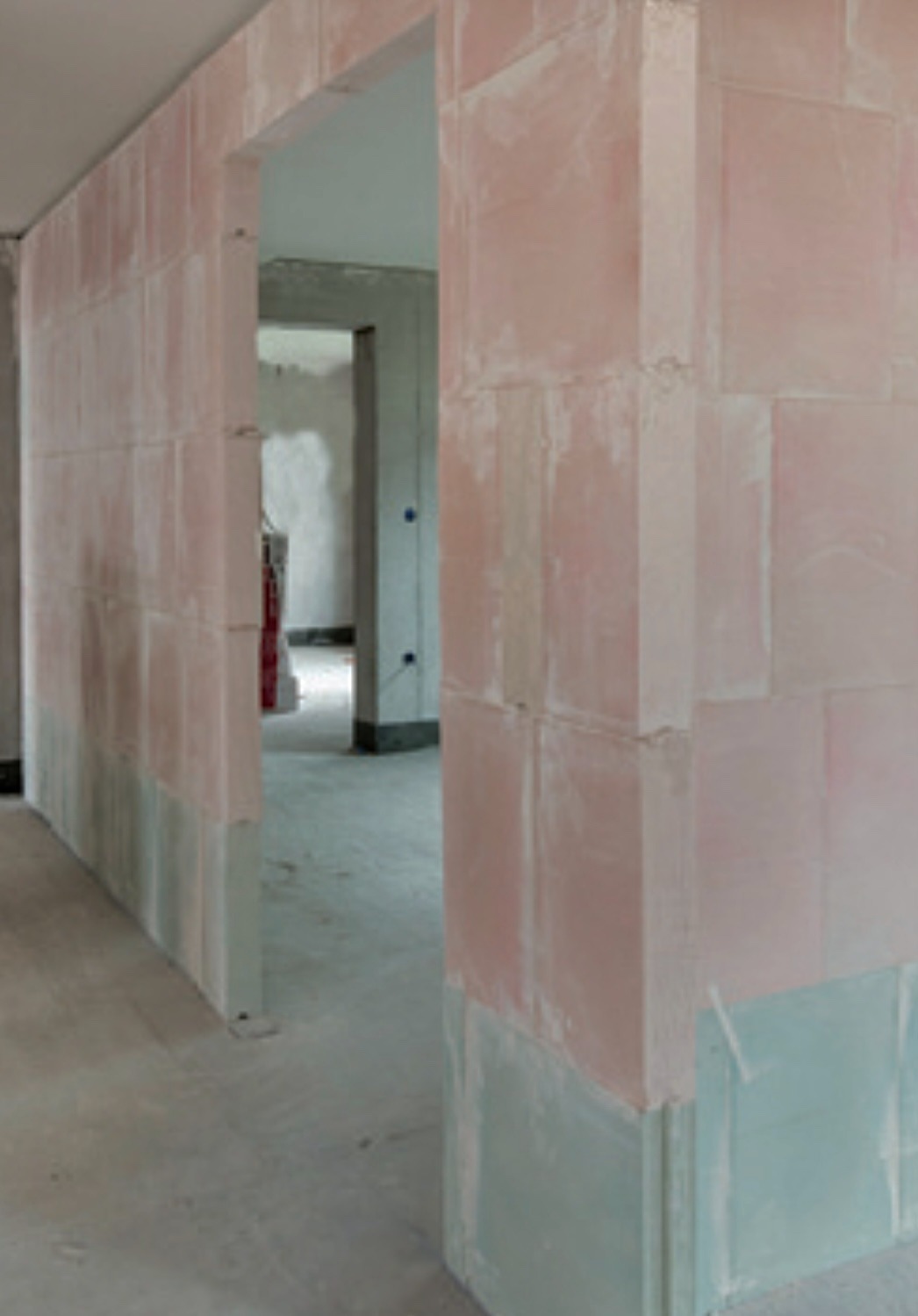 Wnętrze w trakcie murowania ścian z bloków, widoczne surowe ściany z widocznymi spoinami, fragment ościeżnicy oraz podłoga w stanie surowym.