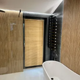 Nowoczesna łazienka z wanną wolnostojącą, grzejnikiem drabinkowym i oknem przesłoniętym żaluzjami z naturalnego drewna bambusowego.