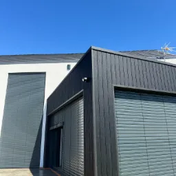 Nowoczesny budynek z szarą elewacją i zewnętrznymi osłonami okiennymi w kolorze szarym, częściowo zasłoniętymi, pod błękitnym niebem, widoczna antena na dachu.