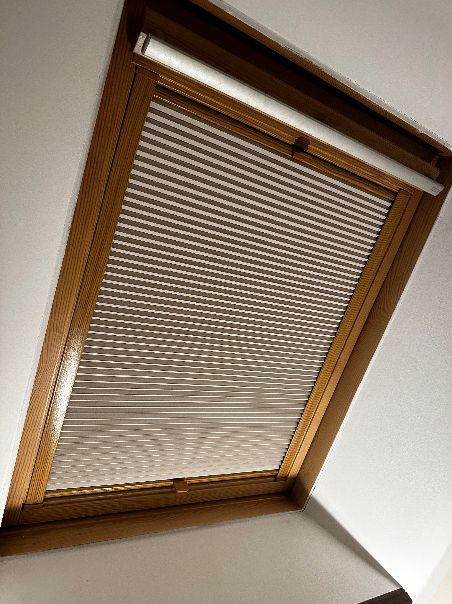 Zamknięta plisowana osłona okienna w drewnianej ramie okna dachowego, widok od dołu.