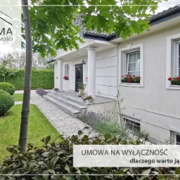 Elegancki, biały dom jednorodzinny z kolumnami przy wejściu, czerwonymi kwiatami w oknach i zadbanym ogrodem. Na pierwszym planie krzewy, w tle żywopłot. W lewym górnym rogu logo agencji...