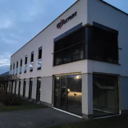 Nowoczesny budynek biurowy z aluminiowymi oknami i fasadą, widok z zewnątrz o zmierzchu, z logo firmy na elewacji.