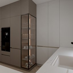 Studio WNĘTRZ Agnieszka Chwedaczuk - Nowoczesna kuchnia w stonowanych barwach: zabudowa z piekarnikiem, przeszklona witryna z oświetleniem LED i zastawą, biały blat z czarną armaturą przy oknie z żaluzjami.