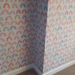 Pokój po odświeżeniu ścian, wykończony tapetą w dziecięce, kolorowe tęcze, z widoczną listwą przypodłogową i narożnikiem.