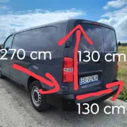Szary bus Peugeot Expert z naniesionymi czerwonymi strzałkami i wymiarami 270 cm długości i 130 cm wysokości oraz głębokości przestrzeni ładunkowej, stojący na szutrowej drodze w słoneczny dzień.
