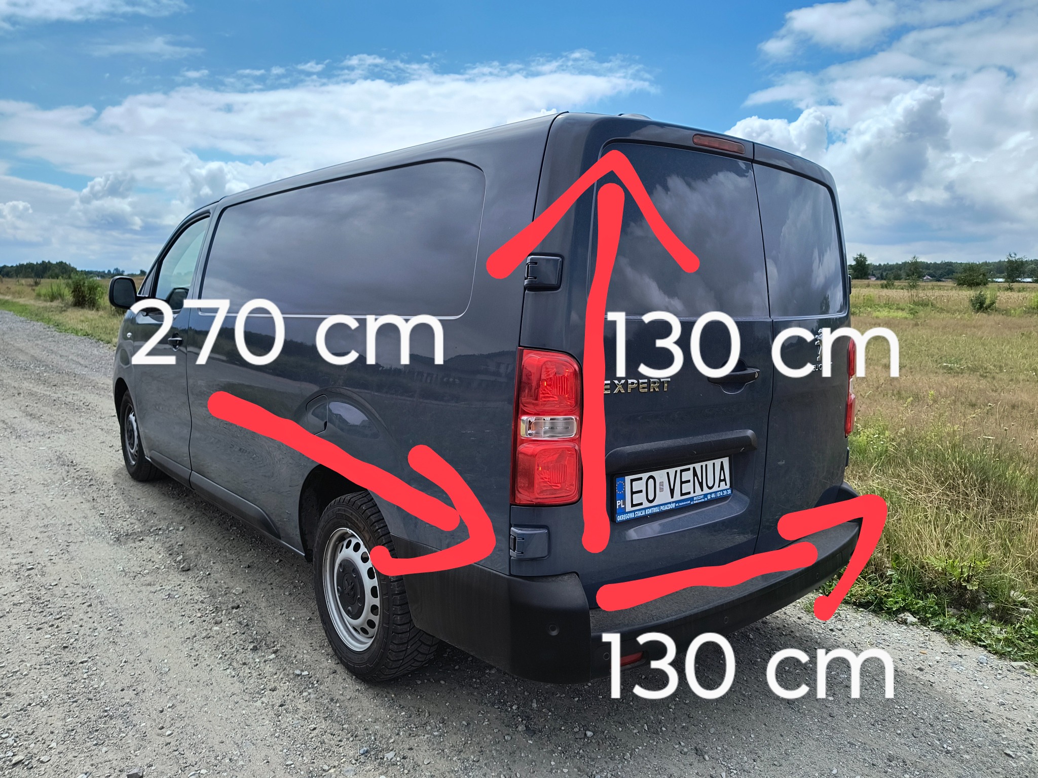 Szary bus Peugeot Expert z naniesionymi czerwonymi strzałkami i wymiarami 270 cm długości i 130 cm wysokości oraz głębokości przestrzeni ładunkowej, stojący na szutrowej drodze w słoneczny dzień.