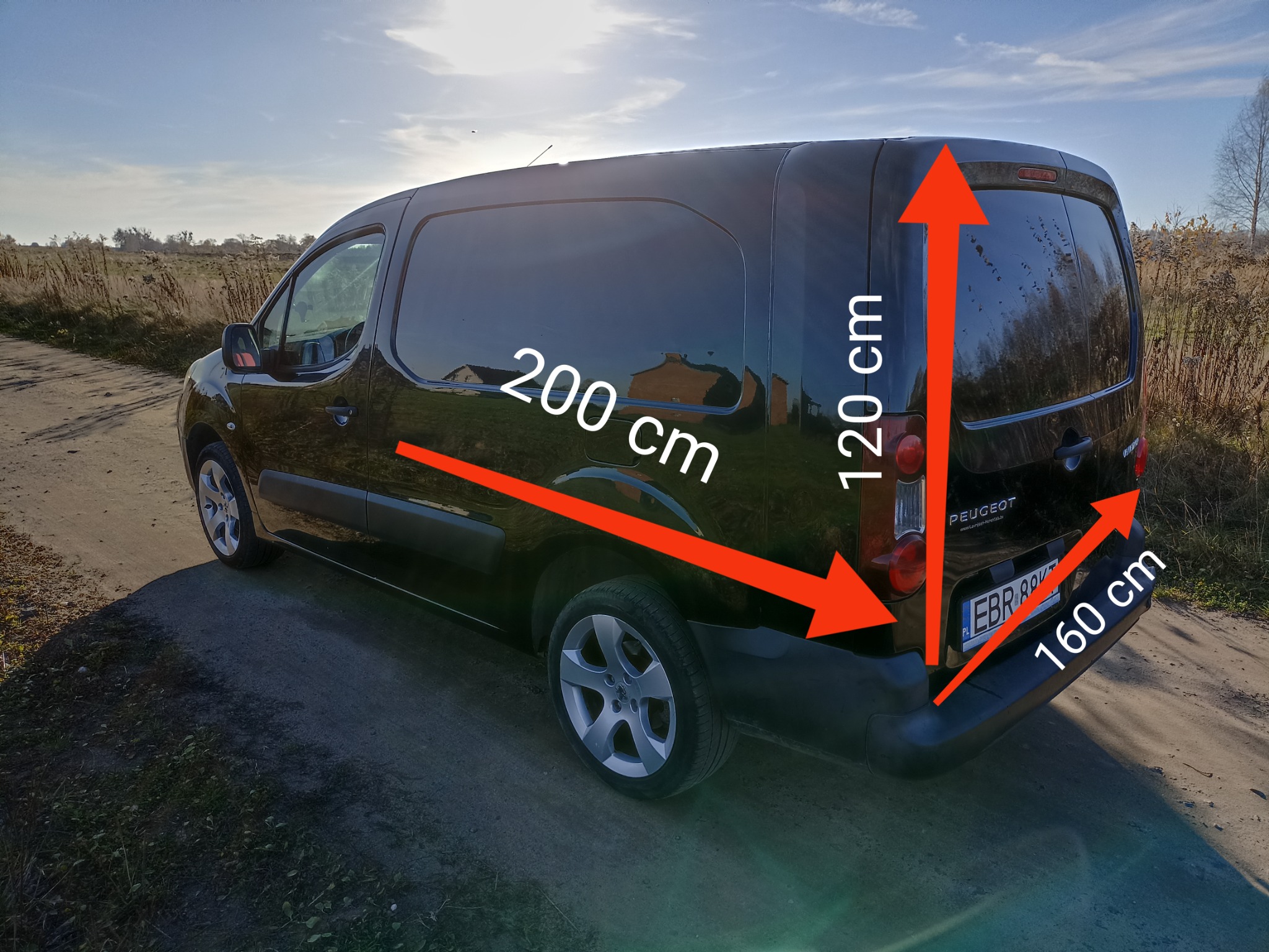 Czarny samochód dostawczy Peugeot Partner z wymiarami: długość 200 cm, wysokość 120 cm, szerokość 160 cm, stojący na polnej drodze w słoneczny dzień.