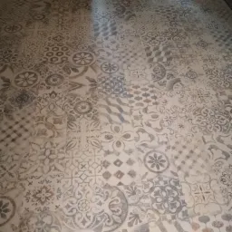 Ułożona podłoga z płytek imitujących patchwork w odcieniach beżu, szarości i bieli, z widocznymi drzwiami w tle.