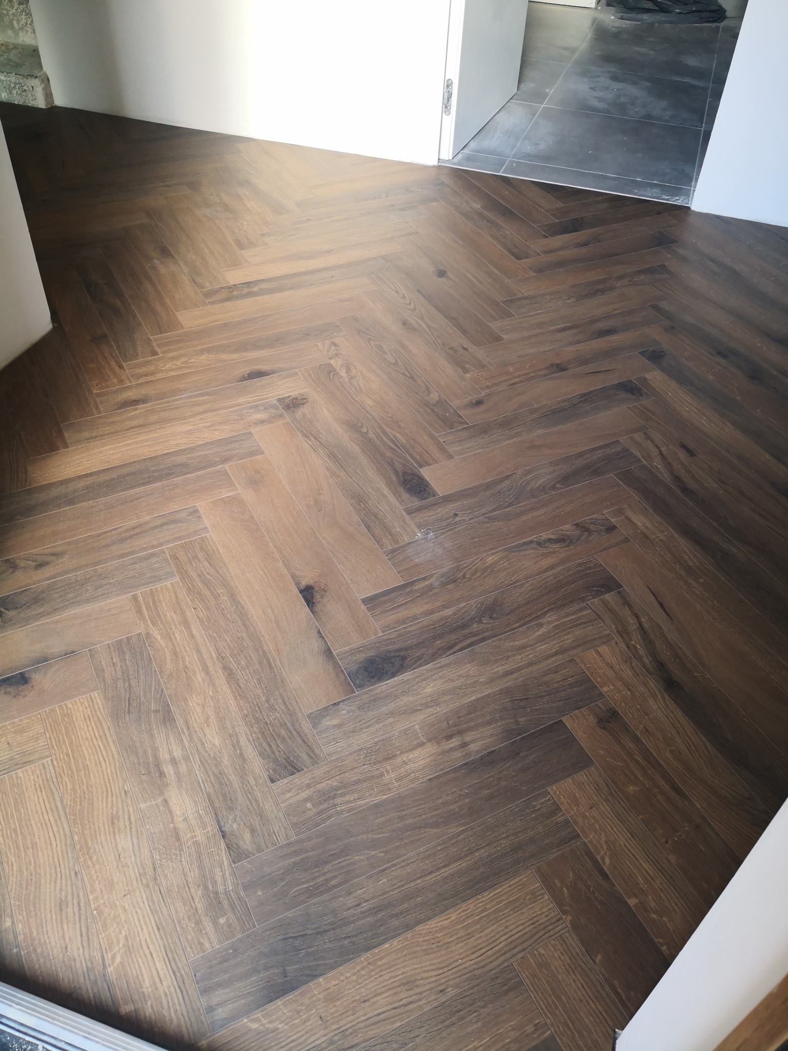 Ukończona podłoga z ciemnobrązowych desek ułożonych we wzór jodełki francuskiej w mieszkaniu w Inowrocławiu, widok z góry na świeżo wykończoną powierzchnię.